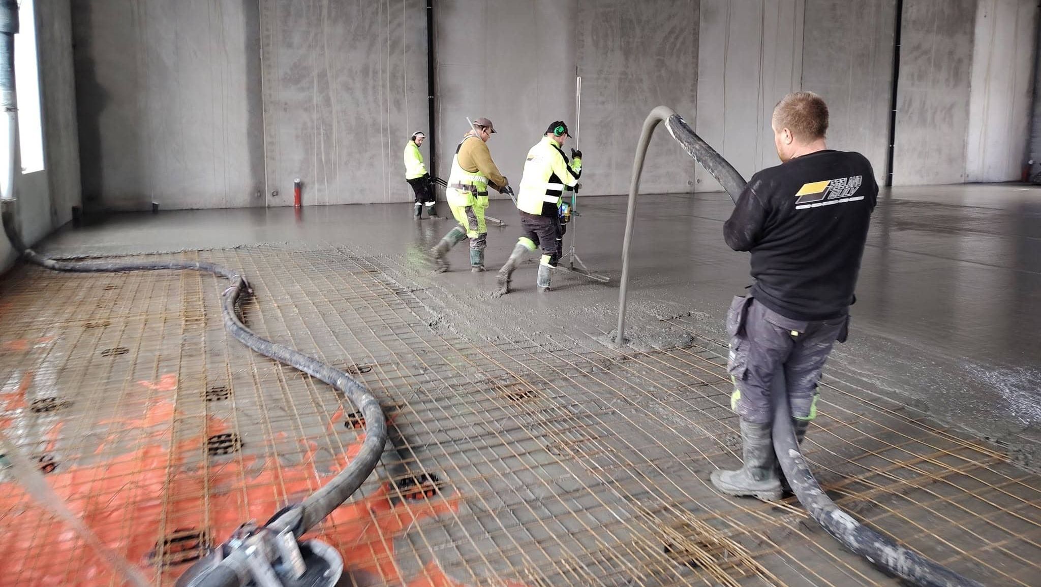 Betongarbeider holder opp rør som punper betong utuover gulv